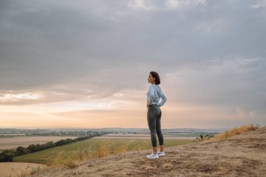 Uçsuz bucaksız bir manzaranın üzerinde huzurlu bir gün batımı yaşayan bir kadın doğanın güzelliğini yansıtır.