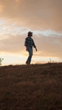 Bir insan gün batımında çimenli bir tepede rengarenk bir gökyüzünün arka planına karşı sakin bir yürüyüşün tadını çıkarıyor.