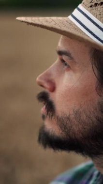 Sakallı ve hasır şapkalı bir adam sakin ve meditasyoncu görünür. Huzurlu bir kırsalın ortasında durur.