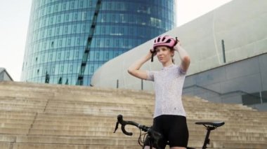 Kararlı bir bisikletçi, modern bir şehir manzarasında heyecan verici bir yolculuğa çıkmadan önce koruyucu kaskını ayarlıyor.
