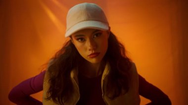 Şık, genç bir birey, canlı bir arka plana karşı modern modayı gözler önüne seren bir şapkayla güven içinde poz verir..