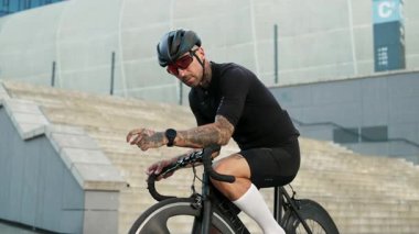 Odaklanmış bir bisikletçi teçhizatını titizlikle ayarlıyor, hem atletizmi hem de şehir yaşam tarzını güzelce gösteriyor.