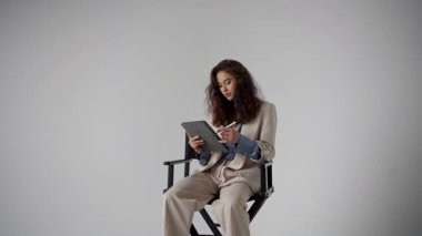 Zarif bir iş elbisesi içindeki genç bir kadın modern ortamda tabletine odaklanmış durumda.