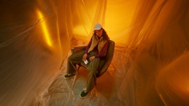 Bir birey, sıcak altın bir ışığa daldırılmış, şeffaf bir yüzeyde oturur.
