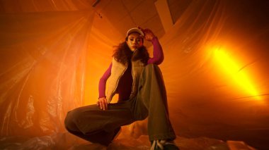 Genç ve yetenekli bir model çarpıcı bir şekilde aydınlatılmış, canlı bir ortamda yaratıcı bir poz verir.