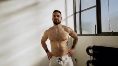 Kendinden emin bir adam fit ve canlı vücudunu parlak, canlı bir spor salonunda gururla sergiliyor.
