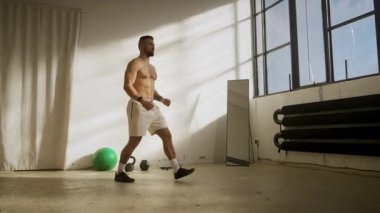 Güçlü bir adam parlak bir spor salonunda egzersiz yapar, gücünü ve kendini spora adadığını gösterir.