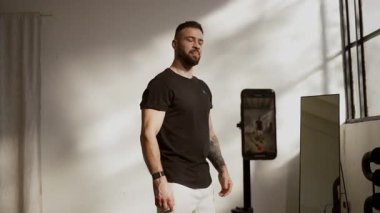 Formda bir adam etkileyici fiziğini parlak bir spor salonunda sergiliyor, fitness 'e bağlılığını gösteriyor.