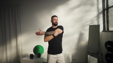 Bir adam canlı ve iyi ışıklandırılmış bir fitness ortamında kollarını uzatır.