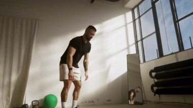 Kendini adamış bir adam güneşli bir spor salonunda spor yapar, spor ve sağlık hedeflerine odaklanır.