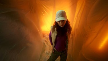 Şık giyimli genç bir kadın dramatik ışıklandırmalı rüya gibi bir ortamda rahatça poz verir.