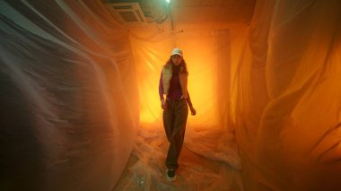 Bir kadın, yumuşak turuncu ışıklarla dolu soyut bir ortamda ustalıkla yol alır.