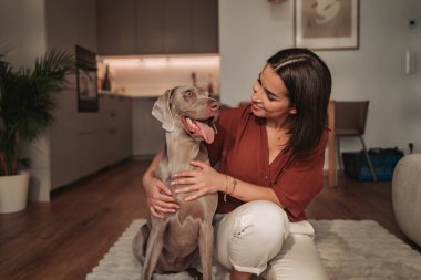 Bir kadın sıcak, sıcak bir oturma odasında sevimli köpeğiyle harika ve sevgi dolu bir anı paylaşıyor.