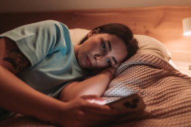 Yatakta dinlenen, telefonuyla meşgul, modern gece alışkanlıkları sergileyen bir kadın..