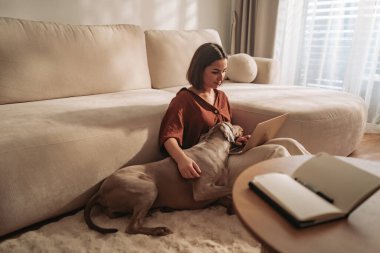 Bir kadın, rahat ve rahat bir oturma odasında köpeğiyle kitap okumaktan hoşlanır.