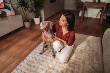 Bir kadın, şık ve rahat bir evde sevgili köpeğiyle mutlu bir şekilde vakit geçirir.