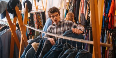 Genç bir adam canlı bir giyim mağazasının içinde şık bir kot pantolon giyiyor.