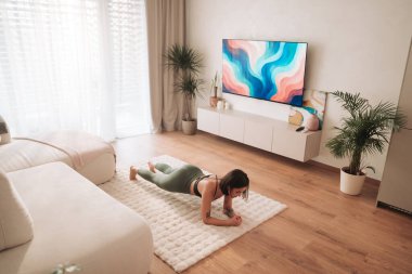 Kendini işine adamış bir insan şık bir oturma odası atmosferinin keyfini çıkarırken tahta egzersizi yapıyor.