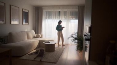 Kadın akıllı evi tabletle kontrol ediyor, modern oturma odasında panjurları indiriyor. 4K video