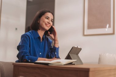 Keyifli genç bir kadın, sıcak ofisinde canlı bir telefon görüşmesi yaparken gülümsüyor.