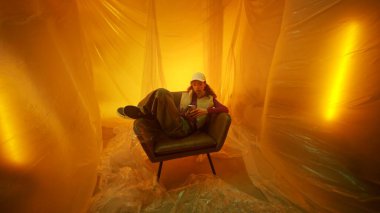 Sıcak, parıldayan sarı perdelerle çevrili, rahat bir koltukta rahatlayan bir birey.