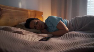 Bir kadın akıllı telefonunun yanında huzur içinde uyuyor, güzel sabahını kucaklıyor.
