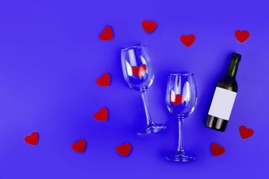 Top view photo of romantic evening, dinner decor hearts love wineglasses with confetti wine bottle on isolated blue background with copyspace