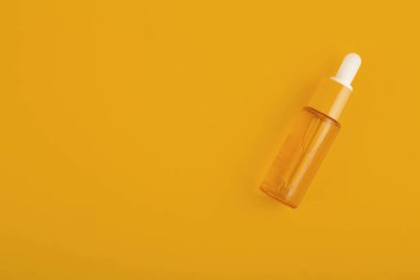 glass yellow bottle with pipette with essential oil on a yellow background top view. Aromatic cosmetic product for skin  hair care Moisturizing beauty product with vitamin C close up
