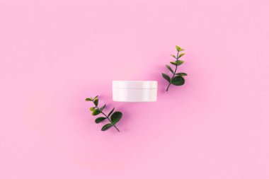 Jar of organic cream with eucalyptus leaves on pink background. Flat lay, top view, copy space. Natural organic product, beauty and spa concep