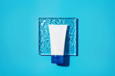 Kadın hijyenik ürün tübü kare üzerine jöle mavisi arkaplan dokusuyla. Şampuan, el kremi, diş macunu beyaz paket yan görünümü. Cilt bakımı, yüz kremi, kopyalama alanı olan nemlendirici kap
