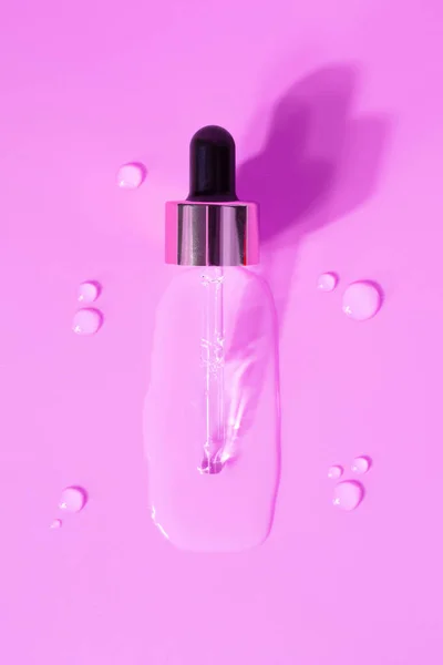 Bottle of drops of anti-aging emulsion and glass pipette on light pink surface close upper view. Skincare and dermatological procedures