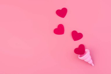 Silikon pembe regl fincanı düz. Kadın sağlığı ve alternatif hijyen. İçinde kan damlaları ya da pembe arka planda kırmızı kalpler olan bir fincan. Çevre dostu, kadın hijyeni için alternatif yeniden kullanılabilir ürün..