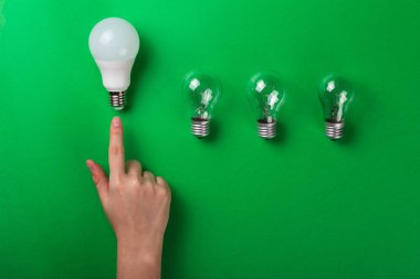 Fikir sahibi erkek el, yeşil arkaplandaki LED ampullere dokunuyor. Fotokopi alanı olan düz bir yer. Ekolojiyi kavra, dünyayı kurtar, fikri, enerjiyi, ekonomiyi, tasarrufu. Dünya günü