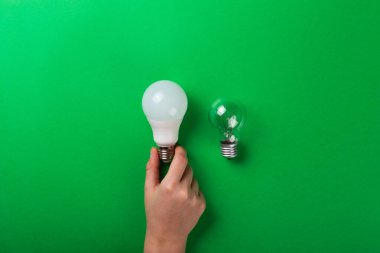 Fikir sahibi erkek el, yeşil arkaplandaki LED ampullere dokunuyor. Fotokopi alanı olan düz bir yer. Ekolojiyi kavra, dünyayı kurtar, fikri, enerjiyi, ekonomiyi, tasarrufu. Dünya günü