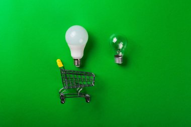 İzole edilmiş yeşil arka planda parlak lambalı alışveriş arabasında öncü lamba. Düz yatıyordu. Ekolojiyi kavra, dünyayı kurtar, fikri, enerjiyi, ekonomiyi, tasarrufu. Dünya günü. Akıllı alışveriş, satış, ama...