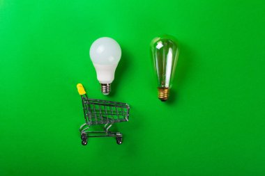 İzole edilmiş yeşil arka planda parlak lambalı alışveriş arabasında öncü lamba. Düz yatıyordu. Ekolojiyi kavra, dünyayı kurtar, fikri, enerjiyi, ekonomiyi, tasarrufu. Dünya günü. Akıllı alışveriş, satış, ama...