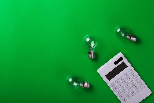 incandescent lamp with white calculator on green background. Energy efficiency concept. Flat lay. Concept ecology, save planet earth, idea, save energy, economy, saving. Earth day