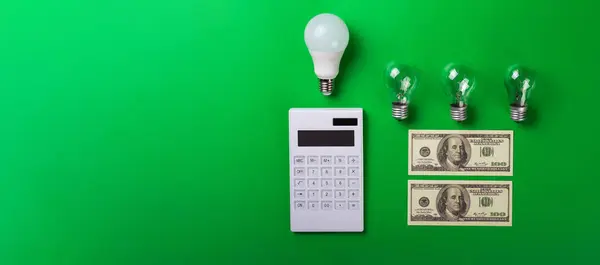 White calculator and incandescent lamps or LED bulb on green background. Concept showing the payment money of electricity bills. savings electricity. Reducing the payment of utility bills