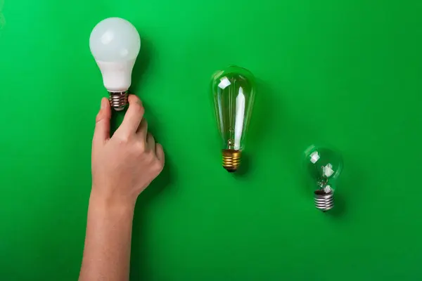 incandescent lamp and hand hold led lamps against on isolated green background. Energy efficiency concept. Flat lay. Concept ecology, save planet earth, idea, save energy, economy, saving. Earth day