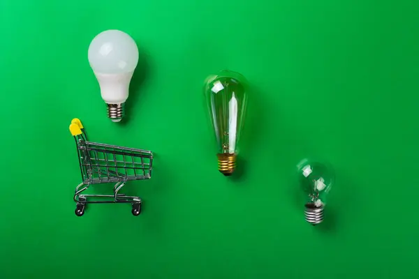 Led lamp in shopping car or incandescent lamp on isolated green background. Flat lay. Concept ecology, save planet earth, idea, save energy, economy, saving. Earth day. Smart shopping, sale, bu