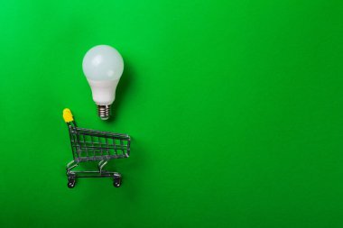 İzole edilmiş yeşil arka planda alışveriş arabasındaki lamba. Düz yatıyordu. Ekolojiyi kavra, dünyayı kurtar, fikri, enerjiyi, ekonomiyi, tasarrufu. Dünya günü. Akıllı alışveriş, satış, ama...