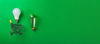 İzole edilmiş yeşil arka planda alışveriş arabasındaki lamba. Düz yatıyordu. Ekolojiyi kavra, dünyayı kurtar, fikri, enerjiyi, ekonomiyi, tasarrufu. Dünya günü. Akıllı alışveriş, satış, ama...