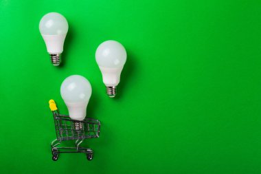 İzole edilmiş yeşil arka planda alışveriş arabasındaki lamba. Düz yatıyordu. Ekolojiyi kavra, dünyayı kurtar, fikri, enerjiyi, ekonomiyi, tasarrufu. Dünya günü. Akıllı alışveriş, satış, ama...