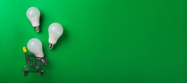 İzole edilmiş yeşil arka planda alışveriş arabasındaki lamba. Düz yatıyordu. Ekolojiyi kavra, dünyayı kurtar, fikri, enerjiyi, ekonomiyi, tasarrufu. Dünya günü. Akıllı alışveriş, satış, ama...