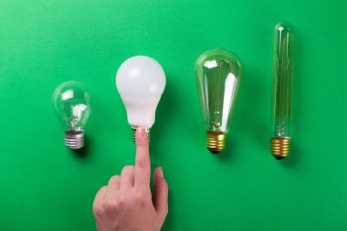 Dişi el seçimi, yeşil arka planda farklı tipte lamba seti oluşturdu. Seçici odaklanma, gürültü. Enerji tasarrufu lambası