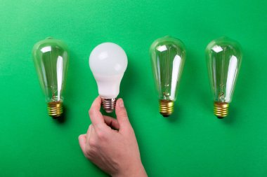Dişi el seçimi, yeşil arka planda farklı tipte lamba seti oluşturdu. Seçici odaklanma, gürültü. Enerji tasarrufu lambası