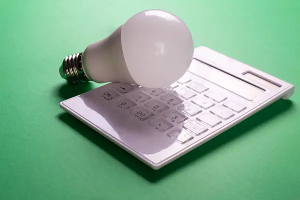White calculator and LED bulb on green background. Concept showing the payment of electricity bills. The concept of savings electricity. Reducing the payment of utility bills
