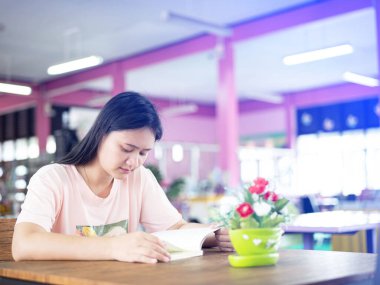 Kitaplarla dolu kütüphanede ders çalışan bir kadın. Eğitim kavramı. Ders arasında, üniversitenin modern iç kütüphanesinde. Kütüphanedeki kitaplıklar arasında kitap seçmek. Masada oturmuş bir şeyler okuyordum.