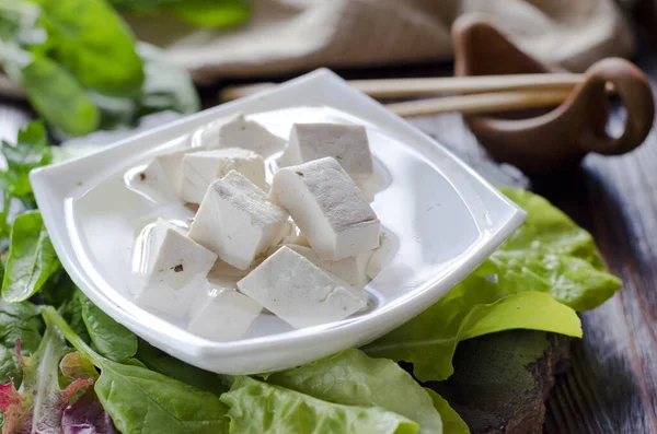 stock image Fresh vegan product - tofu. Soy gray tofu on a plate marinated with spices and salad leaves