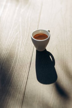 Masada beyaz bir fincan espresso kahvesi var. Güneş ışığı. Kadehteki gölge.